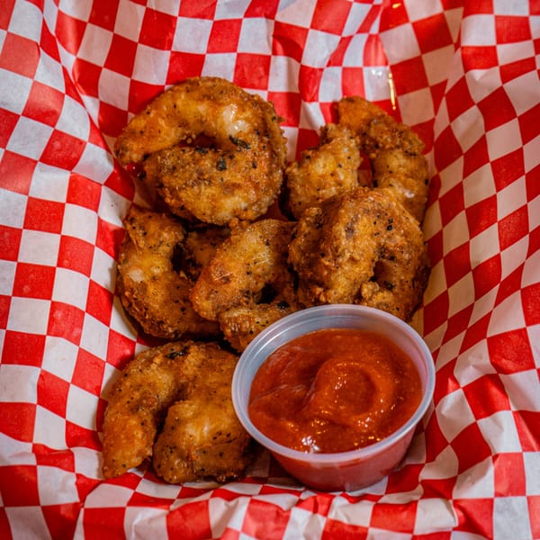 Chicks Chicken fried shrimp with dipping sauce in a red and white checkered basket.