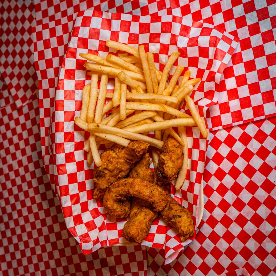 Chicks Chicken's fried chicken tenders and french fries in a red and white checkered basket.